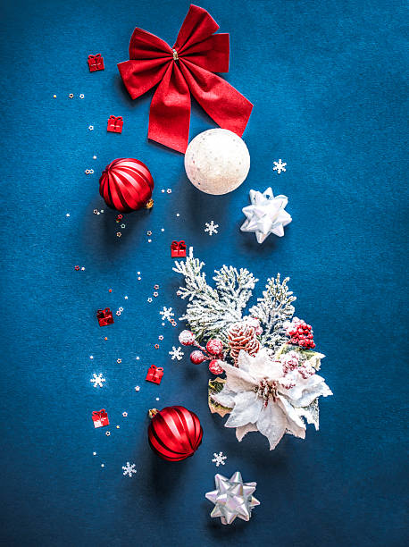 Vertical Christmas flat lay design with red  and white baubles, glitter snowflakes, frosted pine branches, ribbons, Christmas flower, snowflakes and stars confetti, tinsel and red ornaments on blue background. Elegant Christmas banner design