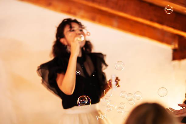 A woman enjoying the activity of blowing bubbles inside a warmly lit room, capturing a playful and carefree atmosphere. The image portrays joy and creativity in a rustic and intimate environment.