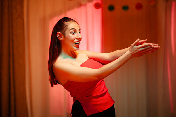 A cheerful woman in a red top claps enthusiastically, expressing joy and excitement in a warmly lit interior filled with vibrant energy.
