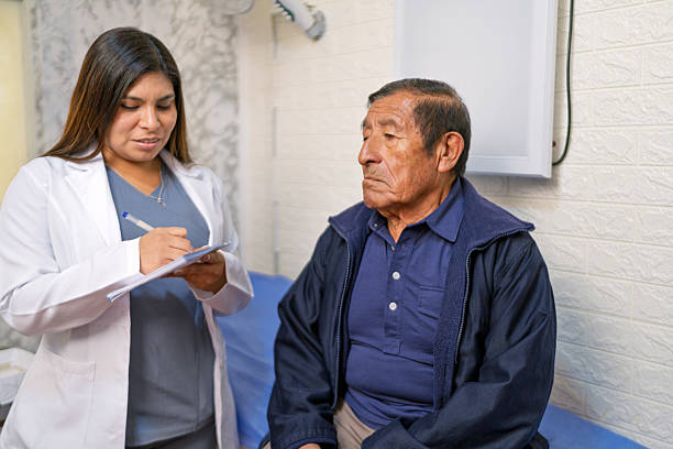 Young female doctor taking notes while examining a senior male patient during a medical consultation in a clinic
