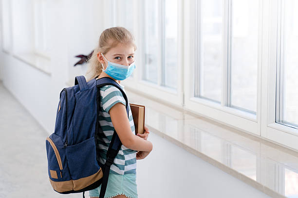istock Kid in protective mask at school inside. Kids back to school. Child with backpack and book 2235653955