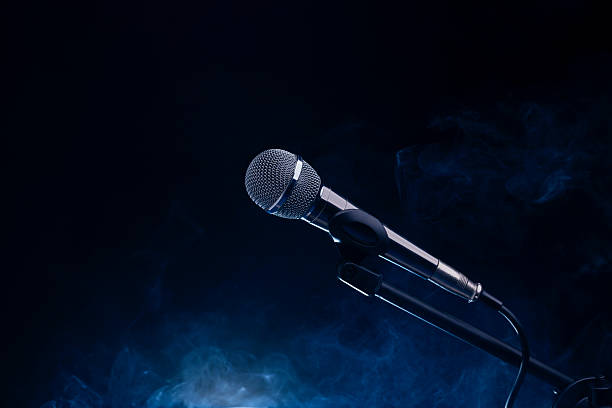 istock Black and silver microphone in studio, on a concert stage with fog and light coming from behind a black and dark background. Professional recording equipment. 2235675176