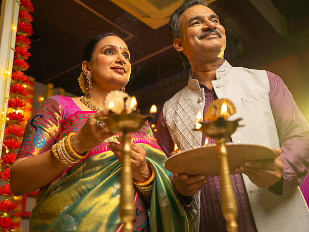 Happy husband and wife in traditional attires burning diyas together while celebrating Diwali festival at home