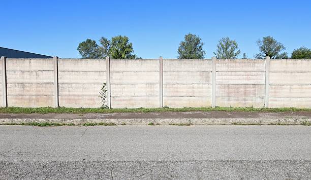 istock Concrete precast compound wall at the road side. Sidewalk and road in front, trees and sky on behind 2235682604