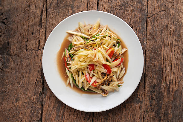 istock Spicy Thai Papaya Salad with Crispy fish on Wooden Table 2235683662