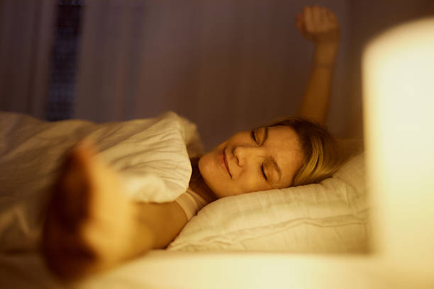 Smiling woman stretching with her eyes closed in a bed.