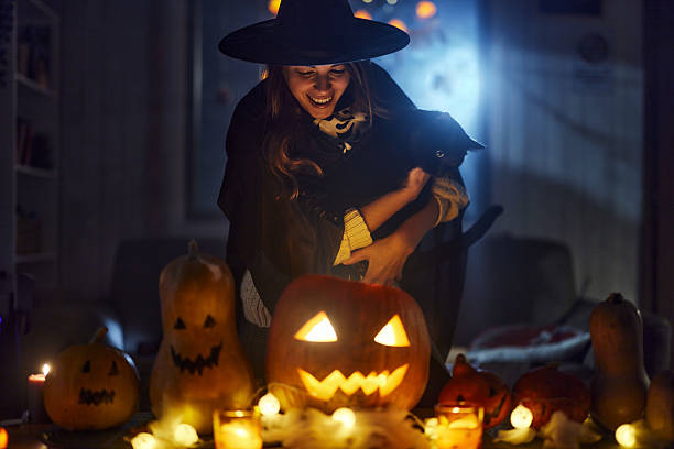 istock Happy witch with black cat looking inside of Jack O' Lantern on Halloween night. 2235685989