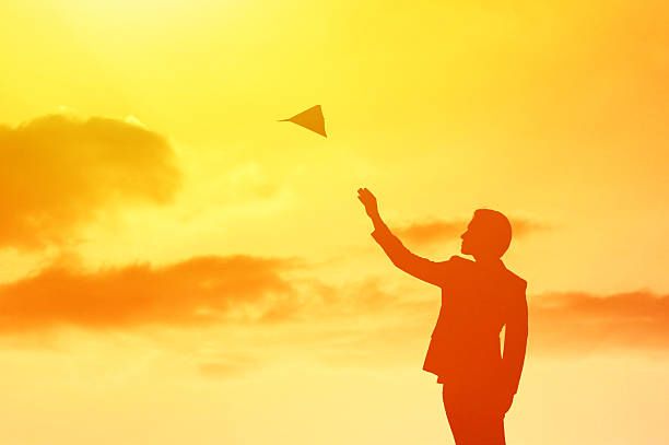 Businessman launching paper airplane into the sky.