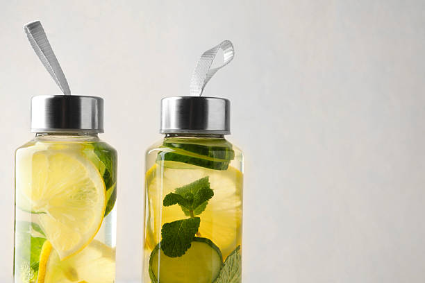 Lemon water with mint and slices of cucumber in bottles on beige background, closeup. Space for text