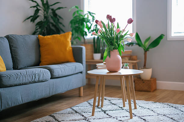 Elegant arrangement of fresh tulips in a vase on a coffee table, with part of a sofa visible in the background, creating a cozy and stylish living room scene.
