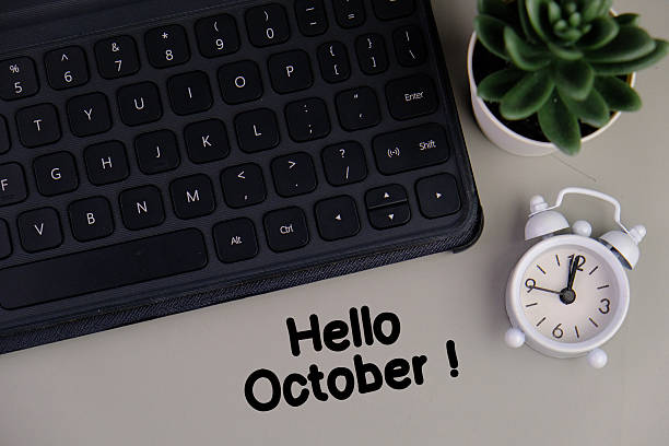 istock text of hello october on table next to computer with  alarm clock. 2235699250