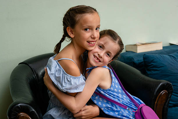 Two young sisters are embracing on a leather sofa, expressing their love and affection