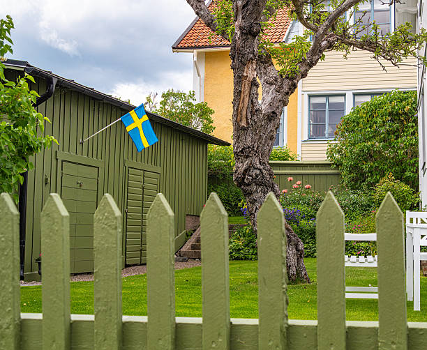 Sigtuna, Sweden - June 9, 2025: A Swedish flag on a green shed in a suburban garden with a yellow house.