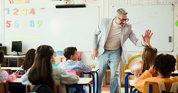 istock Teacher, child and high five for learning in classroom with smile, support or education at school. Mature man, kids and celebration with goals, quiz and happy for success with achievement at academy 2235704537