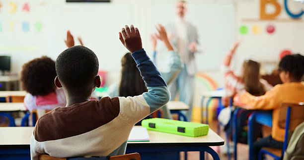 istock Teacher, student and hand up in classroom with children for education, question or answer for knowledge. Man, kids with why or learning for academic growth, future and educator teaching in class 2235704541