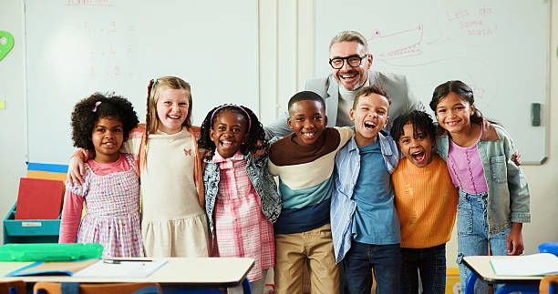 istock Education, hug and portrait of students with teacher in classroom for development or growth. Learning, smile or study with educator man and excited group of kids in class of elementary school 2235704543