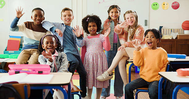istock Education, portrait and children with wave in classroom together for learning, growth or development. Friends, smile and happy student kids in back to school class for excited, knowledge or academics 2235704554