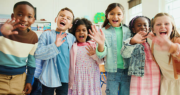 istock Excited, portrait and children with wave in classroom together for learning, growth or development. Friends, smile and happy student kids in back to school class for education, knowledge or academics 2235704583