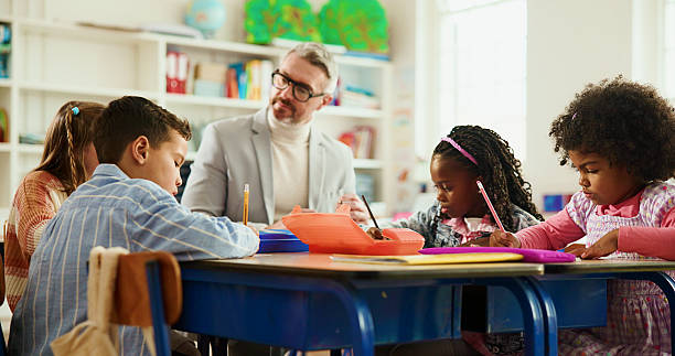 istock Elementary, teacher and man with children, writing or helping students with assignment or education. Knowledge, growth and development of kids in classroom, educator and teaching learner in school 2235704758