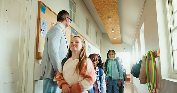 istock Walking, children and teacher at school for welcome, education development or support. Encourage, greeting or group of happy kids with man for learning, scholarship and morning in hallway at academy 2235704794