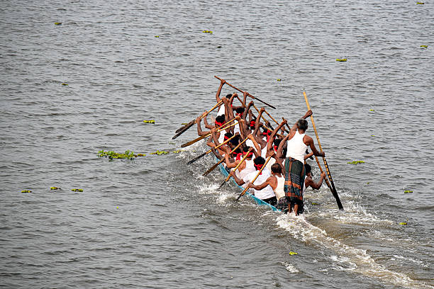 Gazipur, Bangladesh - 7 October, 2020: Rowers in a long wooden boat paddle energetically in unison on a serene lake.