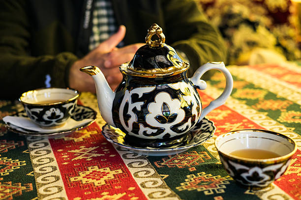 istock Traditional Uzbekistan tea set on a colorful patterned tablecloth, with a person's hands in the background 2235705375