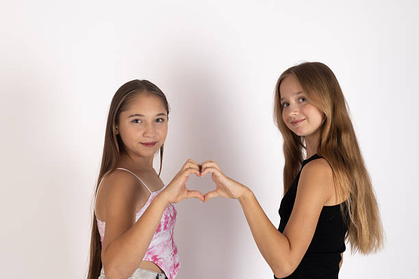 istock Two young girls stand facing each other, forming a heart shape with their hands. 2235706101