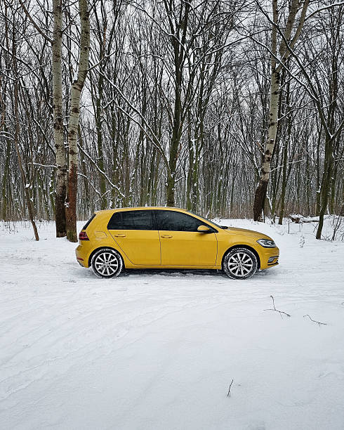 Golden VW hatchback car on a snow-covered road through winter forest. Kyiv, Ukraine - January 14 2024