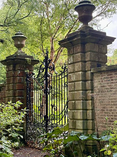 istock An ornate wrought iron gate flanked by tall stone pillars with urn finials, set within a brick wall and surrounded by lush greenery, evoking a sense of grandeur, mystery, and timeless elegance. 2235709743