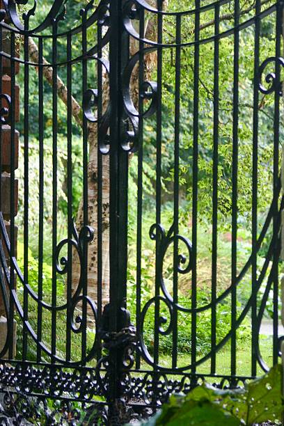 istock An ornate wrought iron gate flanked by tall stone pillars with urn finials, set within a brick wall and surrounded by lush greenery, evoking a sense of grandeur, mystery, and timeless elegance. 2235709757