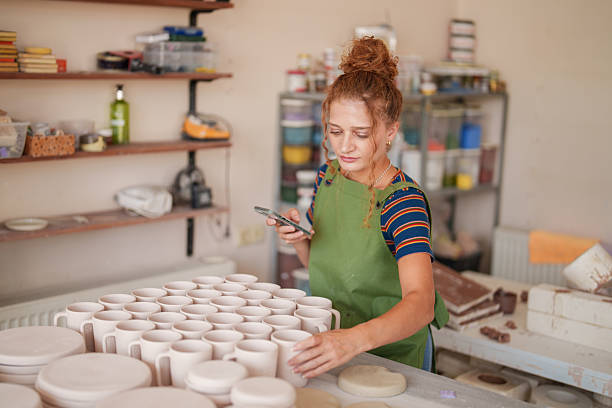 istock Female Potter Inspecting Ceramic Pieces with Smartphone 2235710176