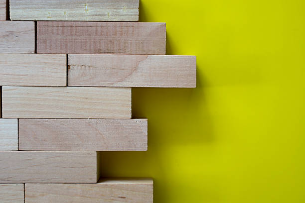 istock Wooden blocks stacked like a wall, with one element sticking out. Placed on a bright yellow background. 2235712293
