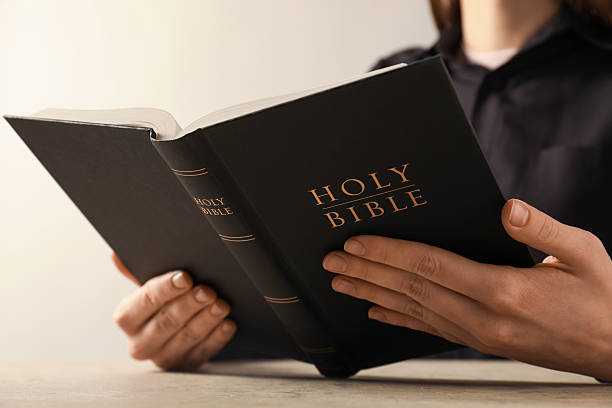 istock Woman reading Holy Bible at beige table, closeup 2235713785