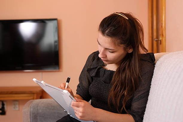 istock Girl sits on sofa writing carefully with marker on board, fully focused on her study task. 2235713964