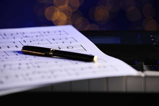 istock Sheet with musical notes and pen on piano against blurred lights, closeup. Bokeh effect 2235717103