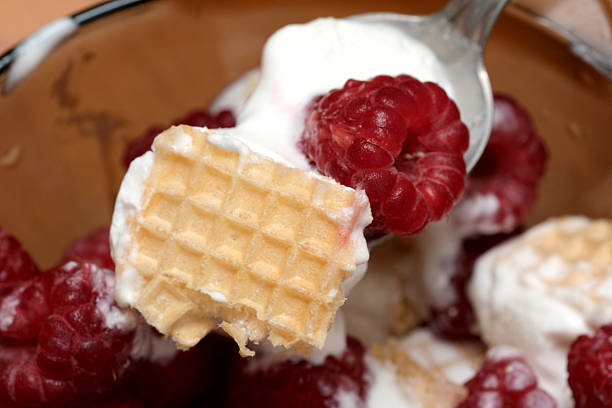 A spoon lifts a morsel of waffle topped with sweet cream and fresh raspberries.
