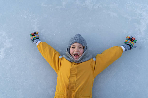 Child having fun in the snow, wearing winter clothing in snowy landscape during daytime. Child with a big smile surrounded by snowy trees and a clear blue sky.