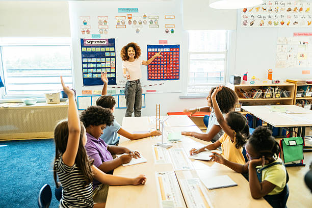 istock Smiling teacher engaging with enthusiastic diverse elementary students raising their hands in a bright, colorful classroom setting 2235721844