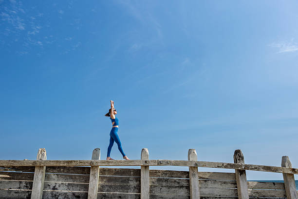 Slender blonde girl doing yoga outside against a blue sky on a sunny day.