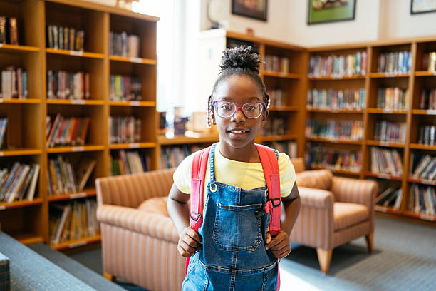 istock Elementary schoolgirl in classroom with schoolbag, looking at camera 2235722876