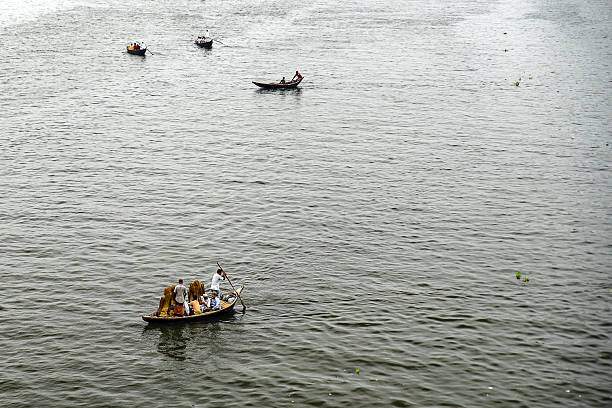 Dhaka, Bangladesh - 28 June, 2019: Boats float across a calm water surface as individuals row and interact with the serene surroundings. A harmonious scene depicting water transport and natural tranquility.