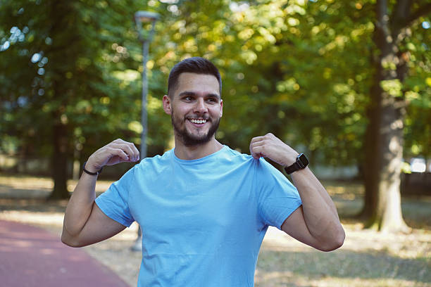 Young man in athletic clothing posing in a park, showing strength and energy after physical activity. The photos capture him drinking water, smiling, stretching, or flexing muscles in natural light and leafy surroundings. Ideal for themes related to healthy living, outdoor workouts, physical fitness, male energy, motivation, and active lifestyle.