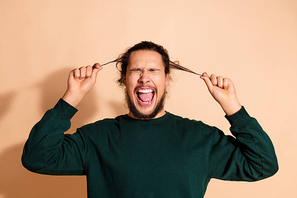 istock Young man in green sweater enthusiastically pulling hair strands while expressing joy against beige background 2235736693