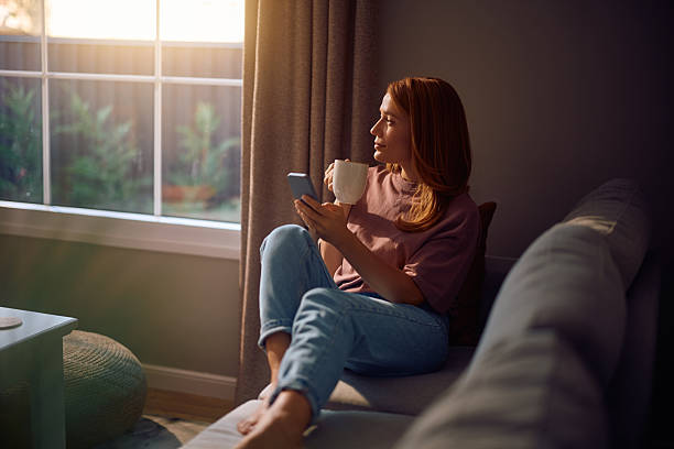 istock Pensive woman using mobile phone while drinking coffee at home. 2235740020
