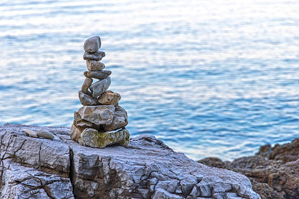 Balanced stone stack by the sea. Zen-inspired stack of balanced stones on a rocky shore with calm blue sea in the background, symbolizing peace and balance