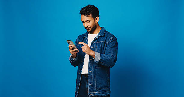 istock Phone, chat and scroll with man in studio for social media, networking and connection. Mockup space, text message and search with person on blue background for contact, typing or communication app 2235745268