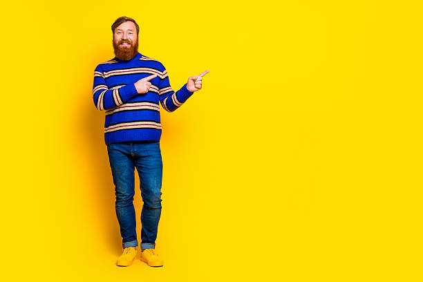 istock Young bearded man pointing with a cheerful expression against a vibrant yellow background in casual fashion 2235748020