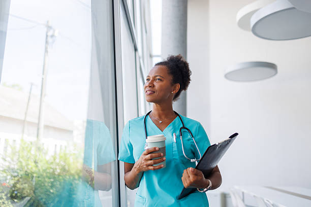 istock Smiling doctor looking out window while holding coffee and clipboard 2235752222