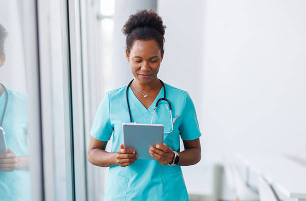 istock Smiling african american nurse using digital tablet in hospital corridor 2235752377