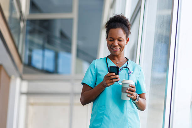 istock Smiling doctor using mobile phone and holding coffee in hospital corridor 2235752505